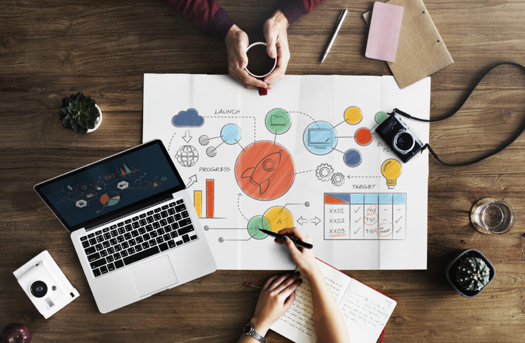 Team di lavoro al tavolo con grafico illustrativo e laptop, impegnati nella pianificazione di una strategia digitale orientata agli obiettivi.