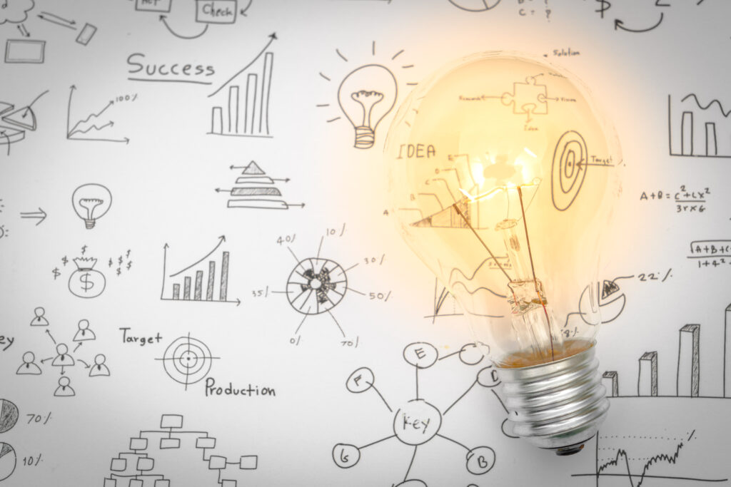 Lampadina accesa davanti a una lavagna con grafici, icone e concetti collegati alla strategia digitale e all’analisi dei dati.